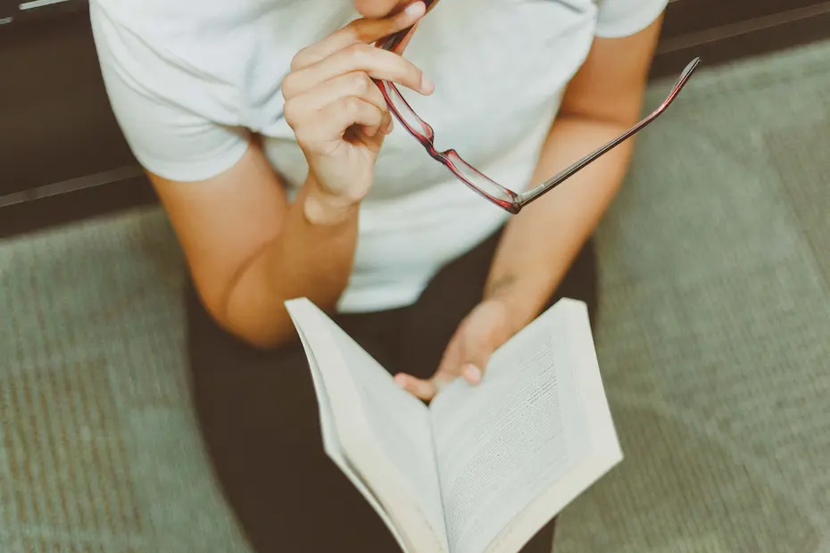 Reading a book while holding an eyeglasses.